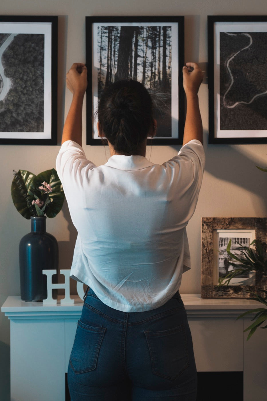 Woman carefully positioning and leveling framed prints on a wall